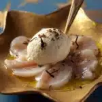 Carpaccio de Saint-Jacques servi avec des herbes fraîches et un filet d'huile d'olive.